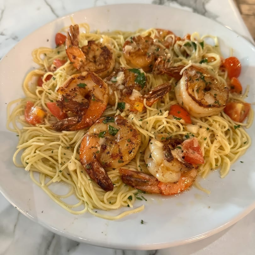 Shrimp scampi with angel hair pasta, cherry tomatoes, and parsley on a white plate.