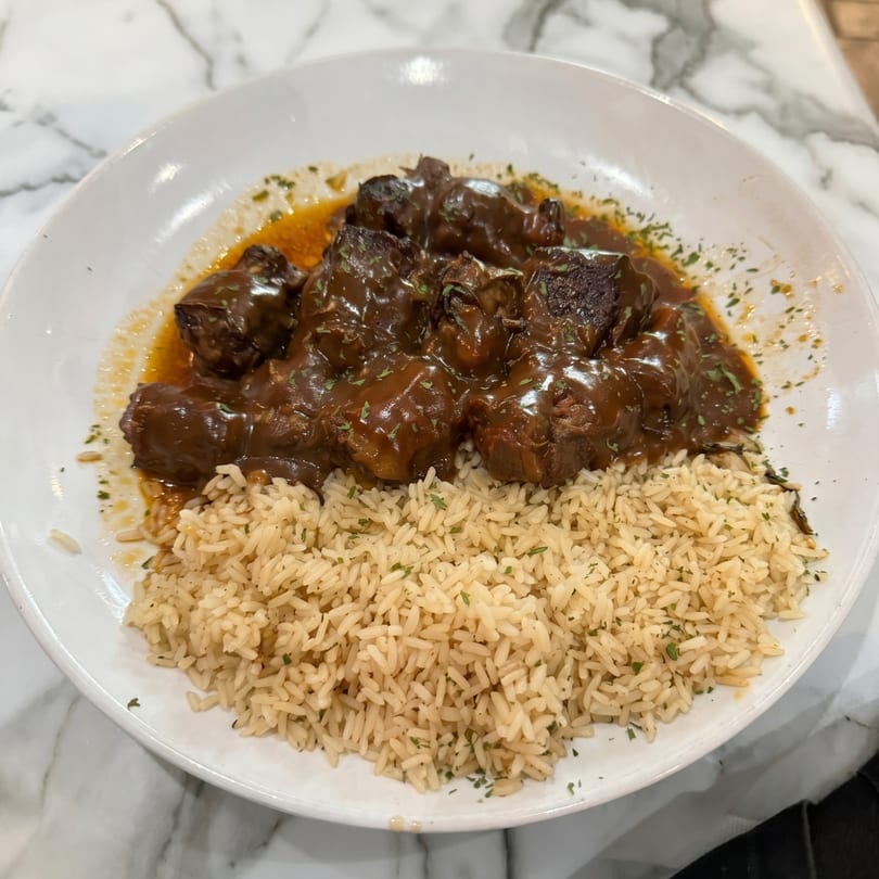 Braised beef in a rich brown sauce with rice, garnished with parsley on a white plate.